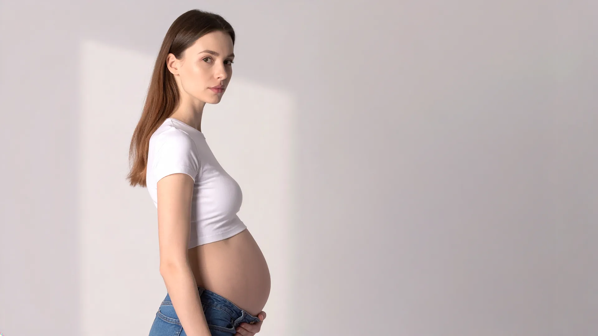 Grūtniece sānu pozā pret gaišu fonu