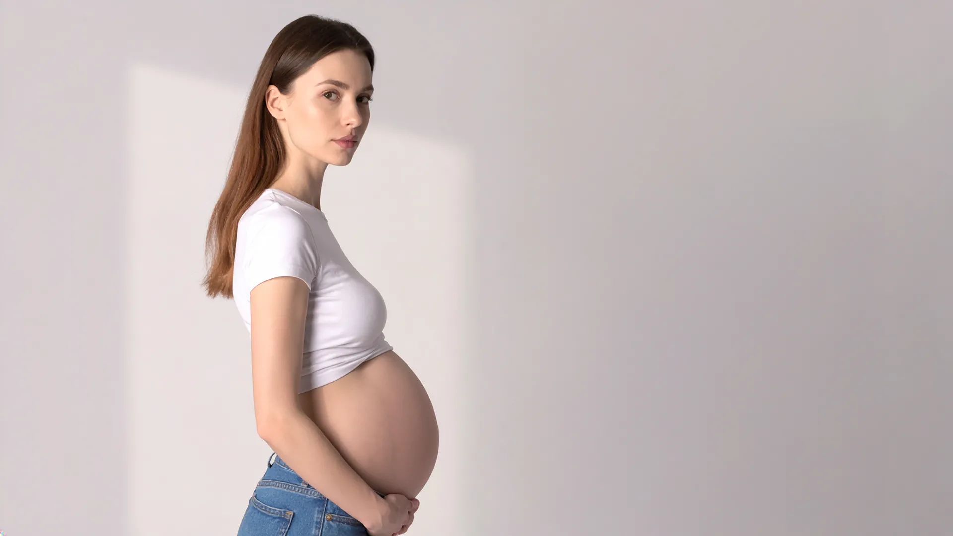 Grūtniece sānu pozā ar roku uz vēdera